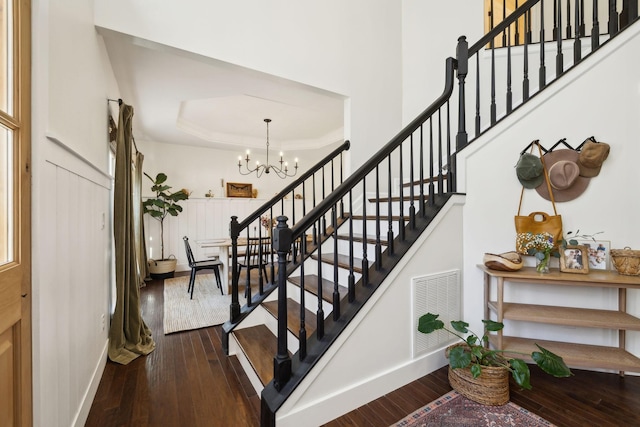 staircase featuring a tray ceiling, a notable chandelier, visible vents, baseboards, and hardwood / wood-style flooring