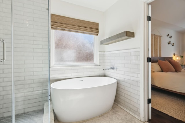 ensuite bathroom with wainscoting, ensuite bath, a freestanding tub, a shower stall, and tile walls