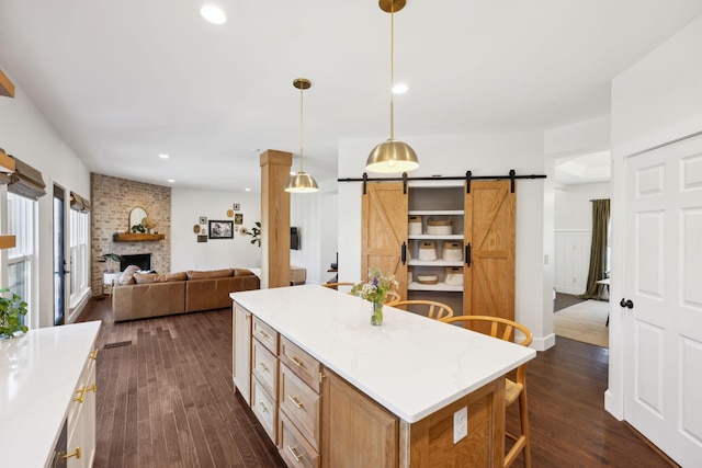 kitchen with dark wood finished floors, hanging light fixtures, a barn door, a brick fireplace, and open floor plan