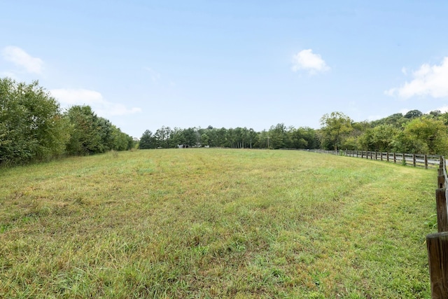 view of yard featuring a rural view, fence, and a view of trees