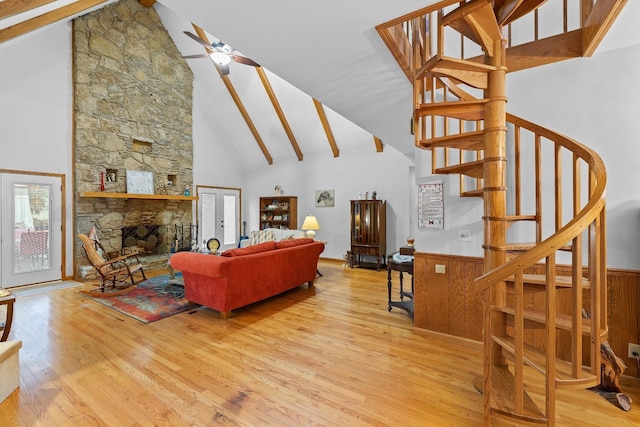 living area featuring a stone fireplace, stairway, wood finished floors, and a ceiling fan