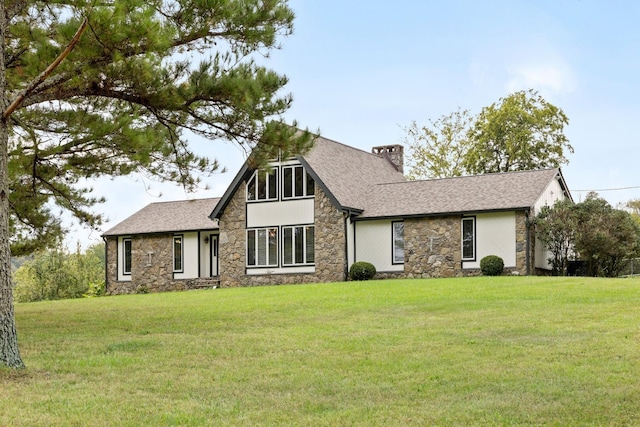 tudor house with a shingled roof, a front yard, a chimney, and stucco siding