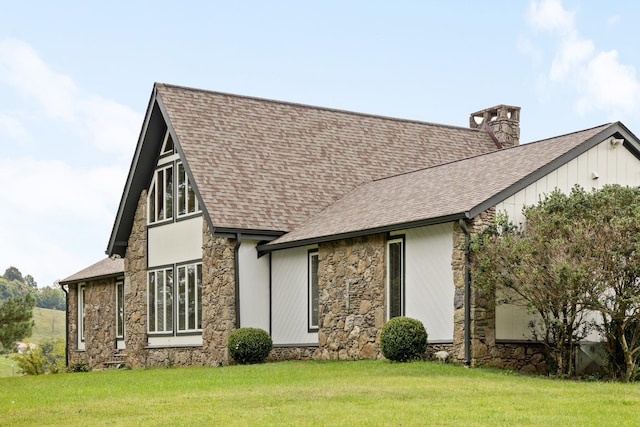 view of front of home featuring a shingled roof, stone siding, board and batten siding, a chimney, and a front yard