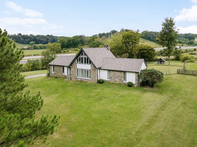 view of front facade featuring stone siding, a shingled roof, fence, and a front yard