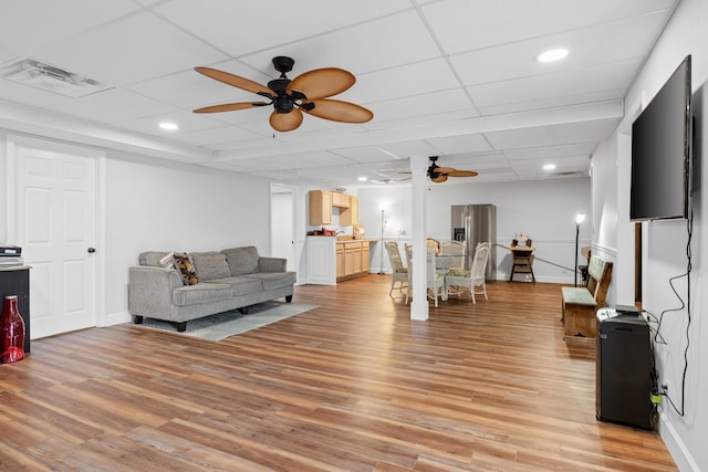 living area featuring ceiling fan, a drop ceiling, light wood-type flooring, and visible vents