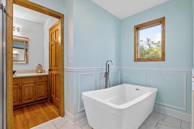 bathroom featuring marble finish floor, a wainscoted wall, a freestanding tub, and vanity