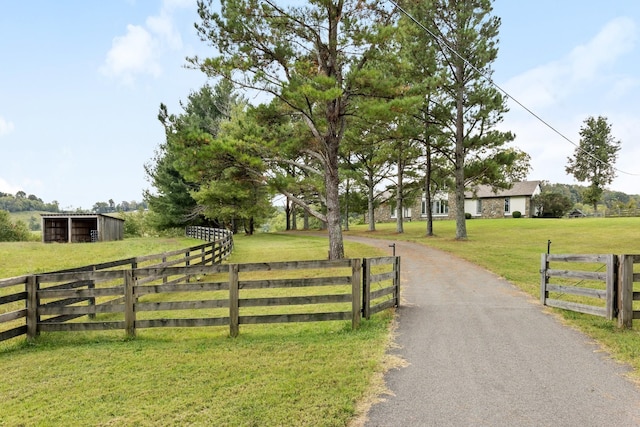 view of gate featuring an outbuilding, a rural view, a lawn, and fence