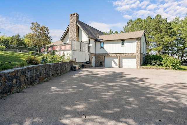 view of home's exterior featuring a garage, stone siding, driveway, and a chimney