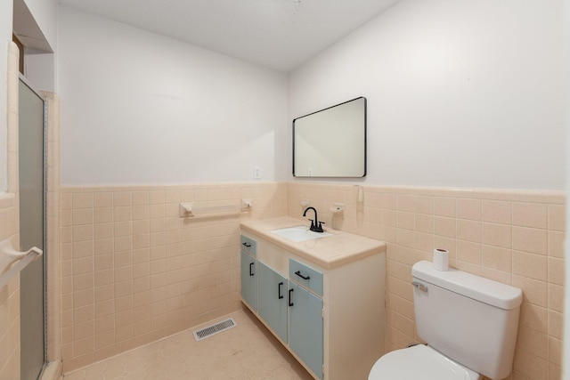 bathroom featuring a wainscoted wall, toilet, visible vents, and tile walls