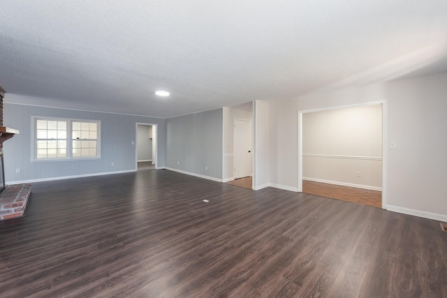 unfurnished living room featuring a brick fireplace, a textured ceiling, baseboards, and dark wood-style flooring