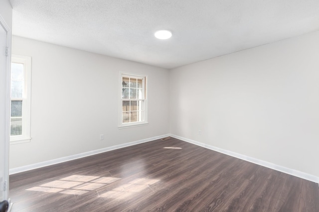 unfurnished room with a textured ceiling, dark wood-type flooring, and baseboards