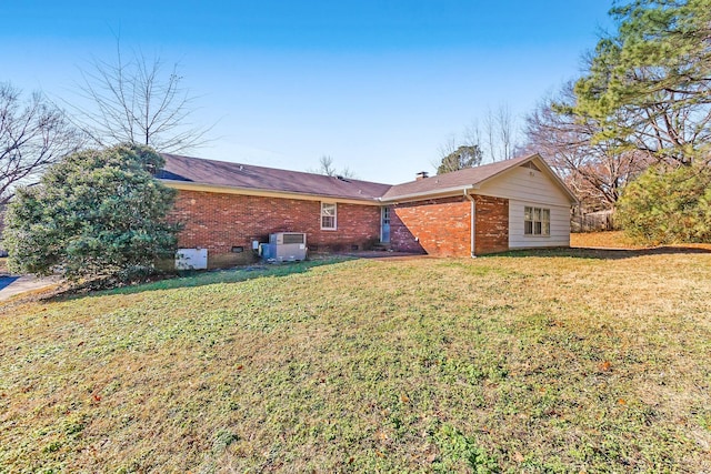 back of house with central air condition unit, a yard, a chimney, and brick siding