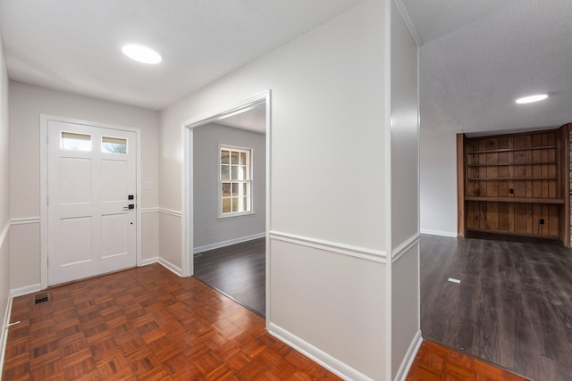 foyer with a textured ceiling, parquet flooring, visible vents, and baseboards