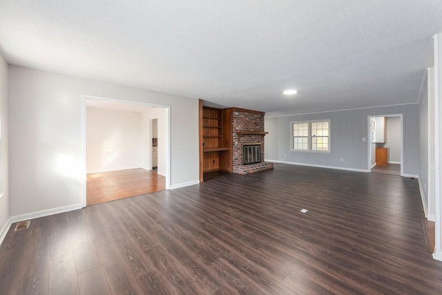 unfurnished living room with a brick fireplace, baseboards, dark wood finished floors, and a textured ceiling