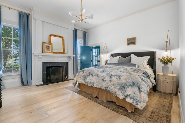 bedroom featuring a high end fireplace, a notable chandelier, crown molding, and wood finished floors