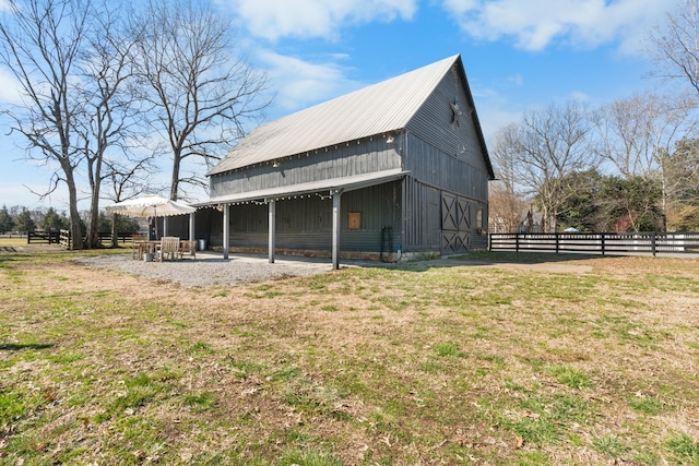 view of side of property featuring a patio, an outdoor structure, a barn, fence, and a yard