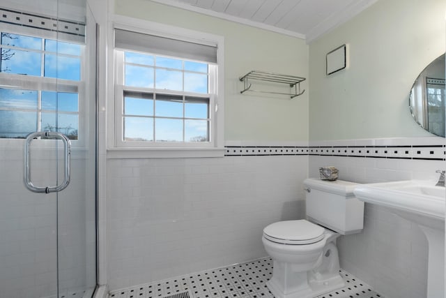 bathroom featuring tile walls, toilet, ornamental molding, wainscoting, and a shower stall