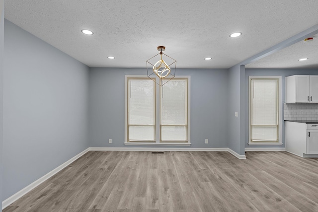 unfurnished dining area featuring light wood-type flooring, baseboards, and a textured ceiling