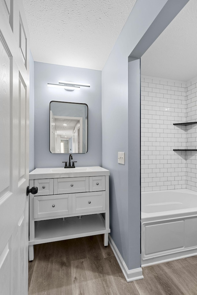 full bath featuring baseboards, a textured ceiling, vanity, and wood finished floors