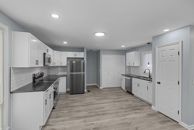 kitchen featuring dark countertops, light wood-style floors, appliances with stainless steel finishes, and a sink