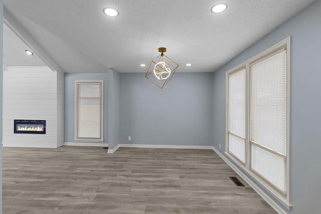 unfurnished room with a textured ceiling, a fireplace, wood finished floors, and baseboards