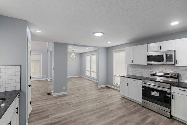 kitchen with stainless steel appliances, light wood finished floors, dark countertops, and white cabinetry