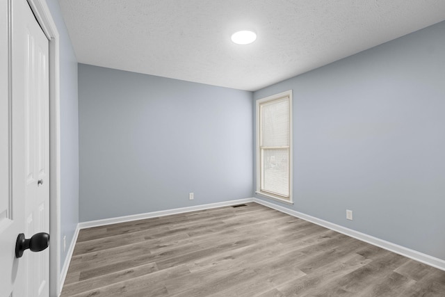 unfurnished bedroom featuring a textured ceiling, wood finished floors, visible vents, baseboards, and a closet