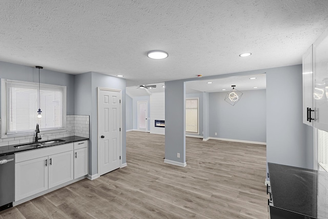 kitchen featuring light wood-style flooring, a fireplace, a sink, stainless steel dishwasher, and dark countertops