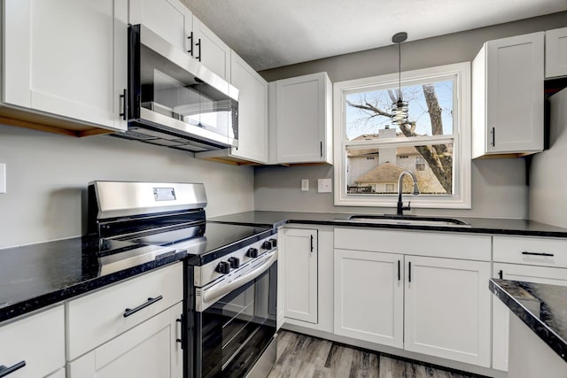 kitchen featuring light wood finished floors, stainless steel appliances, hanging light fixtures, white cabinetry, and a sink