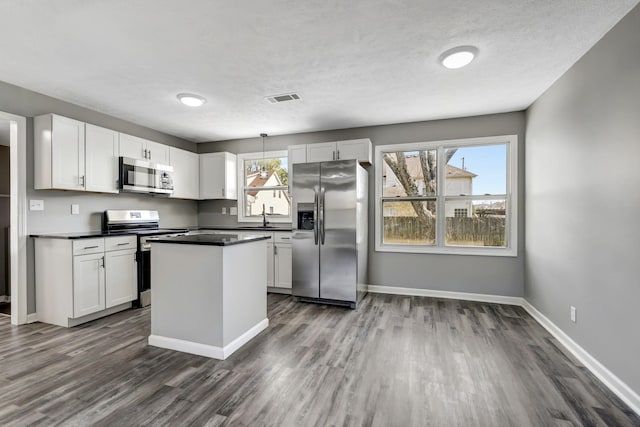 kitchen featuring visible vents, dark countertops, stainless steel appliances, white cabinetry, and a sink