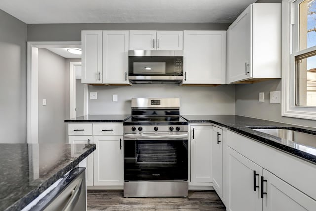 kitchen with dark stone countertops, appliances with stainless steel finishes, white cabinets, and dark wood-style flooring