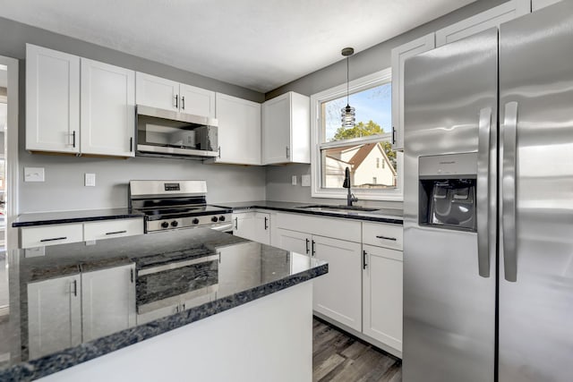 kitchen featuring pendant lighting, dark wood finished floors, appliances with stainless steel finishes, white cabinetry, and a sink