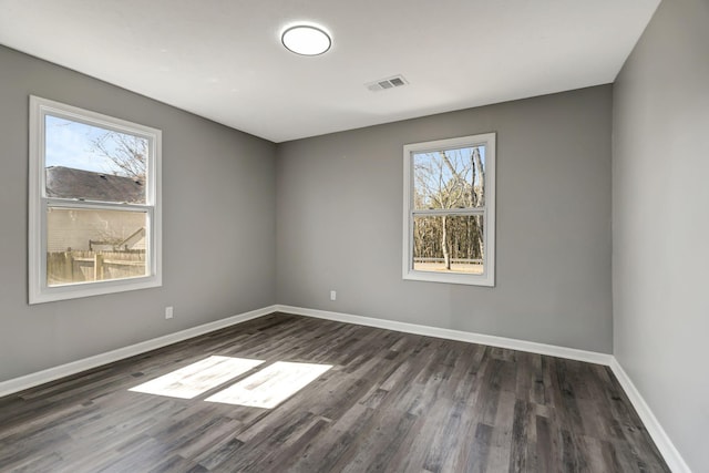 unfurnished room with dark wood-type flooring, visible vents, plenty of natural light, and baseboards