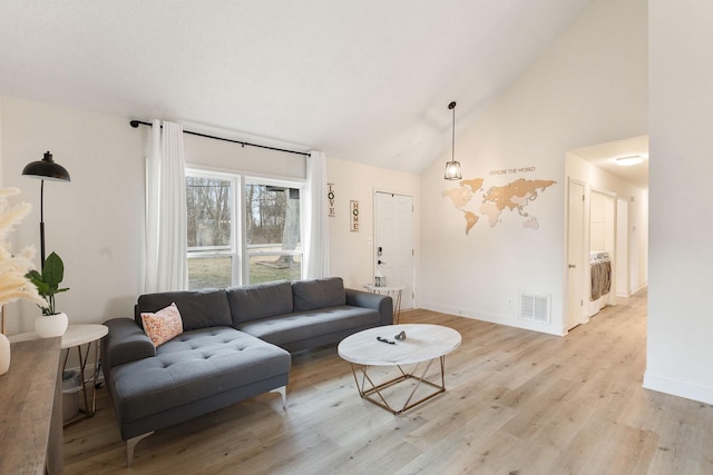 living area with high vaulted ceiling, visible vents, baseboards, light wood-style floors, and washer / dryer