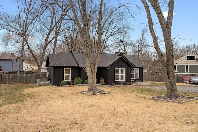 view of front of house with a shingled roof, central AC unit, board and batten siding, a front yard, and fence