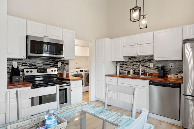 kitchen featuring stainless steel appliances, separate washer and dryer, a sink, white cabinets, and wooden counters