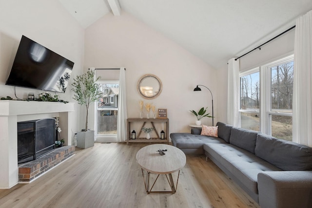 living area with a brick fireplace, beam ceiling, a wealth of natural light, and wood finished floors