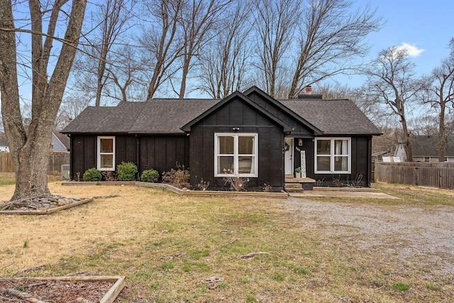 view of front of house with a shingled roof, a chimney, fence, board and batten siding, and a front yard