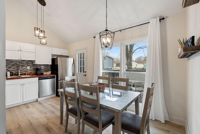 dining space featuring light wood-style floors, vaulted ceiling, and baseboards