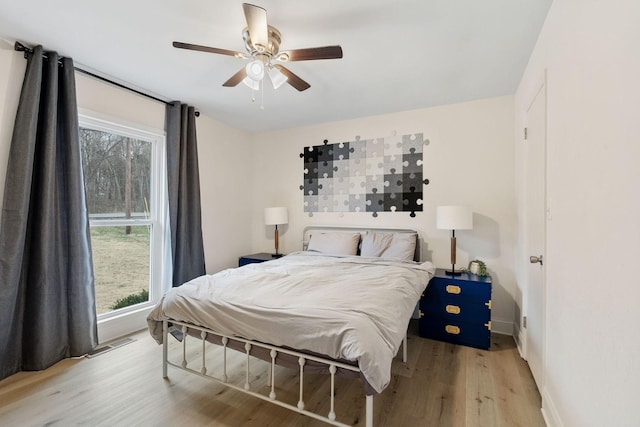 bedroom with light wood-type flooring, ceiling fan, visible vents, and baseboards