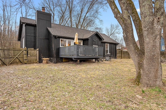 back of house featuring a lawn, a chimney, roof with shingles, fence, and a deck