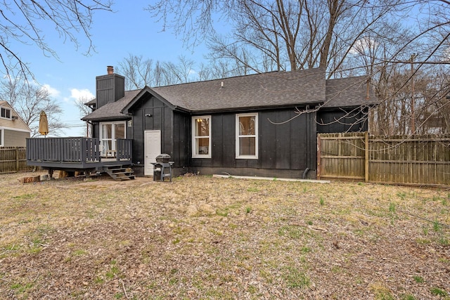 back of house featuring a chimney, roof with shingles, fence, a deck, and board and batten siding