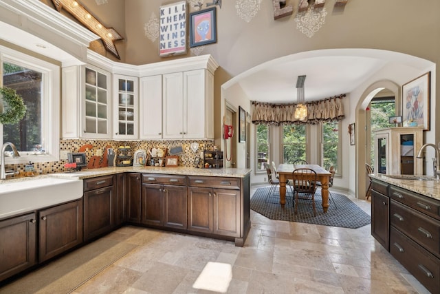 kitchen with a towering ceiling, decorative backsplash, white cabinets, and a sink