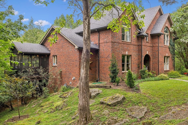 view of front of home with a sunroom, a shingled roof, brick siding, and a front yard