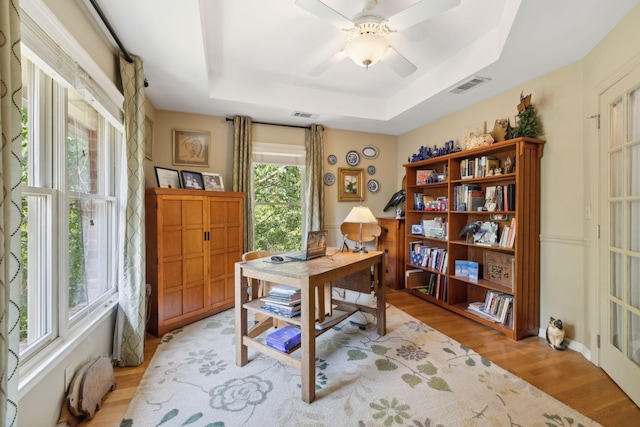 office with a ceiling fan, a raised ceiling, visible vents, and light wood finished floors