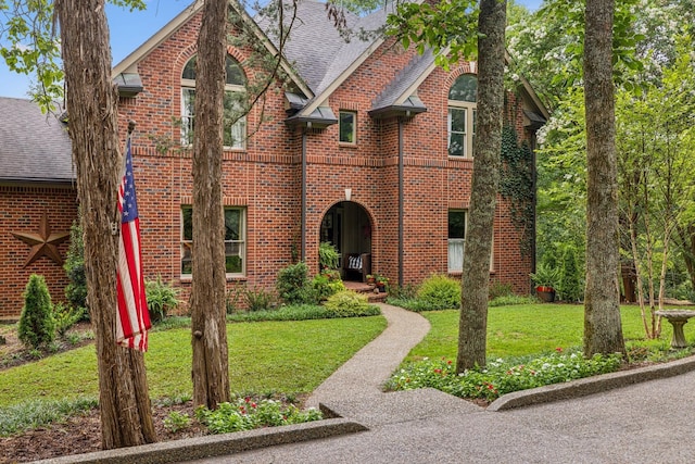 english style home with brick siding, roof with shingles, and a front lawn