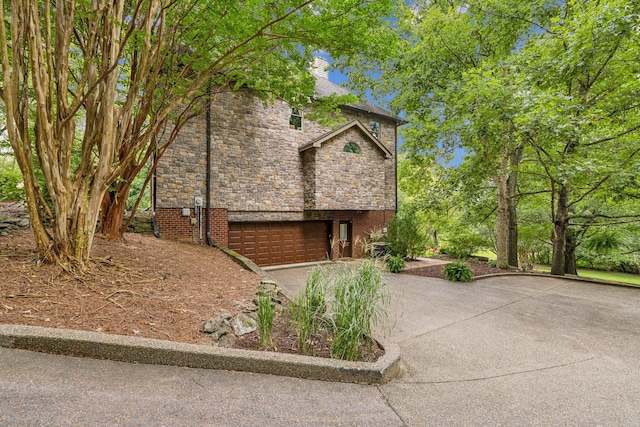 view of property exterior with an attached garage, driveway, a chimney, and stone siding