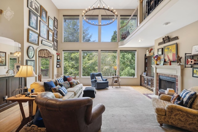 living room with arched walkways, a towering ceiling, wood finished floors, an inviting chandelier, and a fireplace