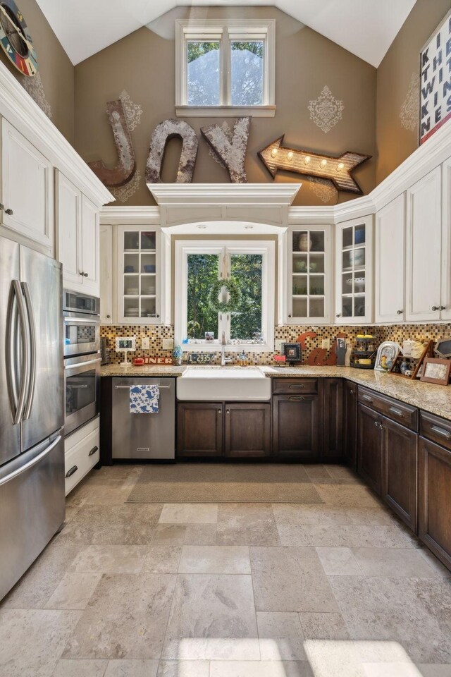 kitchen with dark brown cabinetry, tasteful backsplash, appliances with stainless steel finishes, high vaulted ceiling, and a sink