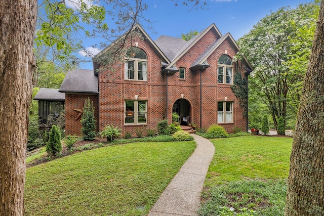 view of front of home featuring a shingled roof, a front yard, and brick siding